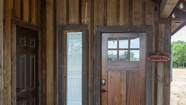 A rustic wooden building with a dark brown door and a sign reading "The Painted Bunting." - Painted Bunting Cabin (15 MIN to Magnolia/Baylor) (Elm Mott)