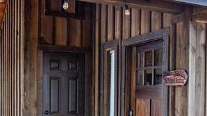 A rustic wooden building with a dark wooden door and a sign reading "The Painted Bunting." - Painted Bunting Cabin (15 MIN to Magnolia/Baylor) (Elm Mott)