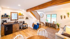 A spacious living area with a kitchen, wooden beams, a staircase, and a dining area. - The Nuthatch Cabin (15 MIN to Magnolia & Baylor) (Elm Mott)