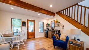 A spacious living area with a wooden staircase, a dining table with chairs, a blue sofa, and a kitchen area with a window. - The Nuthatch Cabin (15 MIN to Magnolia & Baylor) (Elm Mott)