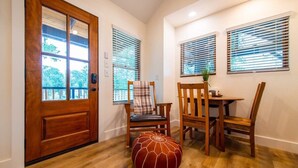 A room with a wooden door, two windows with blinds, a table with chairs, and a red ottoman. - The Sparrow Treehouse 15 MIN to Magnolia & Baylor (Elm Mott)