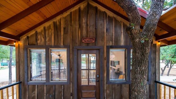 Una rustica baita di legno con un portico in legno, una porta con una finestra e un cartello con su scritto 'The Warbler'.