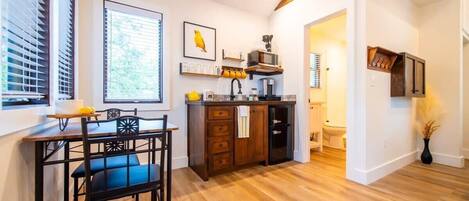 A modern kitchen with wooden cabinetry, a dining area with a table and chairs, and a view of the adjacent bathroom.
