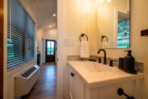 A bathroom with a white sink, black faucet, and a mirror above it. There is a towel rack with a white towel hanging on it. - The Starling Treehouse 15 MIN to Magnolia & Baylor (Elm Mott)