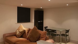 Een moderne woonkamer met een bruine leren bank, een eettafel met vier stoelen en een boekenkast.