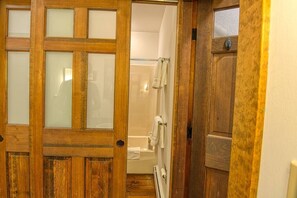 Une porte en bois donne accès à une salle de bain équipée d’une douche, d’un porte-serviettes et d’un radiateur.