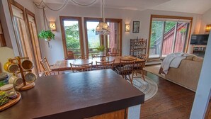 Een ruime keuken met een centraal eiland, een houten eettafel en stoelen. Er is een groot raam met uitzicht op groen.