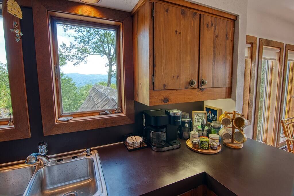 A kitchen with a large window, wooden cabinets, a coffee maker, and various kitchen items on the counter.