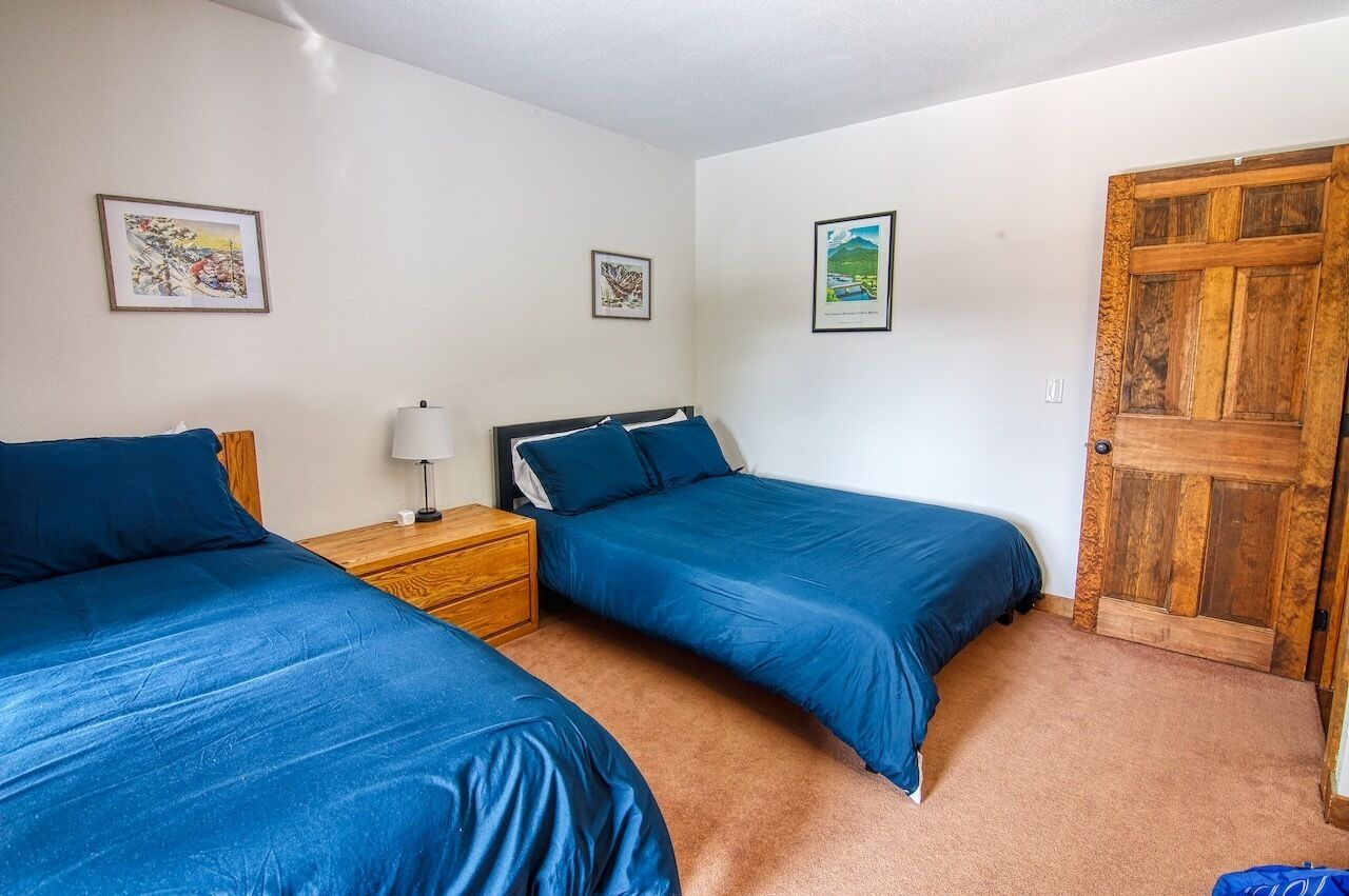 Quarto com duas camas, uma mesa de cabeceira de madeira e uma porta.