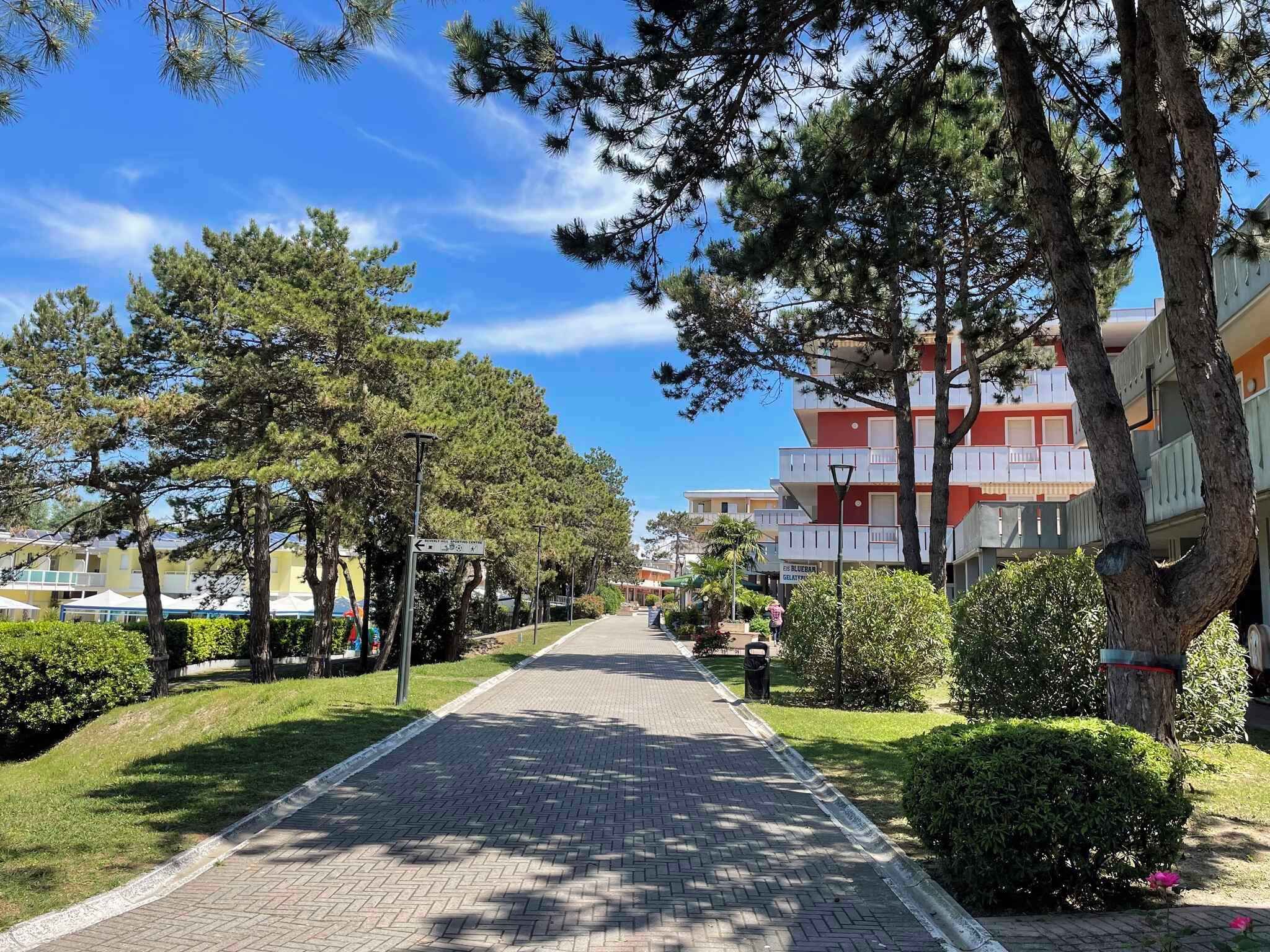 A paved pathway lined with trees and a building with balconies.