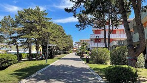 A paved pathway lined with trees and a building with balconies. - Holiday apartment Spacious, close to the sea, with air conditioning (Bibione)