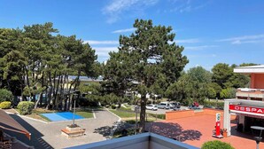 A view of a parking area with trees, a blue play area, and a building with a red sign. - Holiday apartment Spacious, close to the sea, with air conditioning (Bibione)
