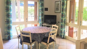 Een eetgedeelte met een ronde tafel, vier stoelen, een televisie en een foto aan de muur.