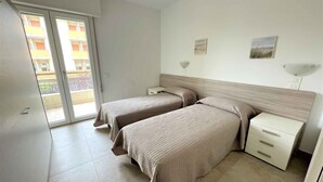 Ein Schlafzimmer mit zwei Betten, einer Glastür zum Balkon und einem kleinen Nachttisch mit Lampe.
