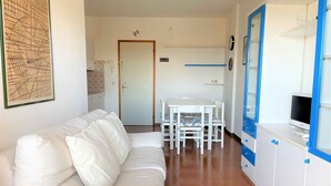 Un sofá blanco, una mesa de comedor con sillas y un televisor sobre un mueble.