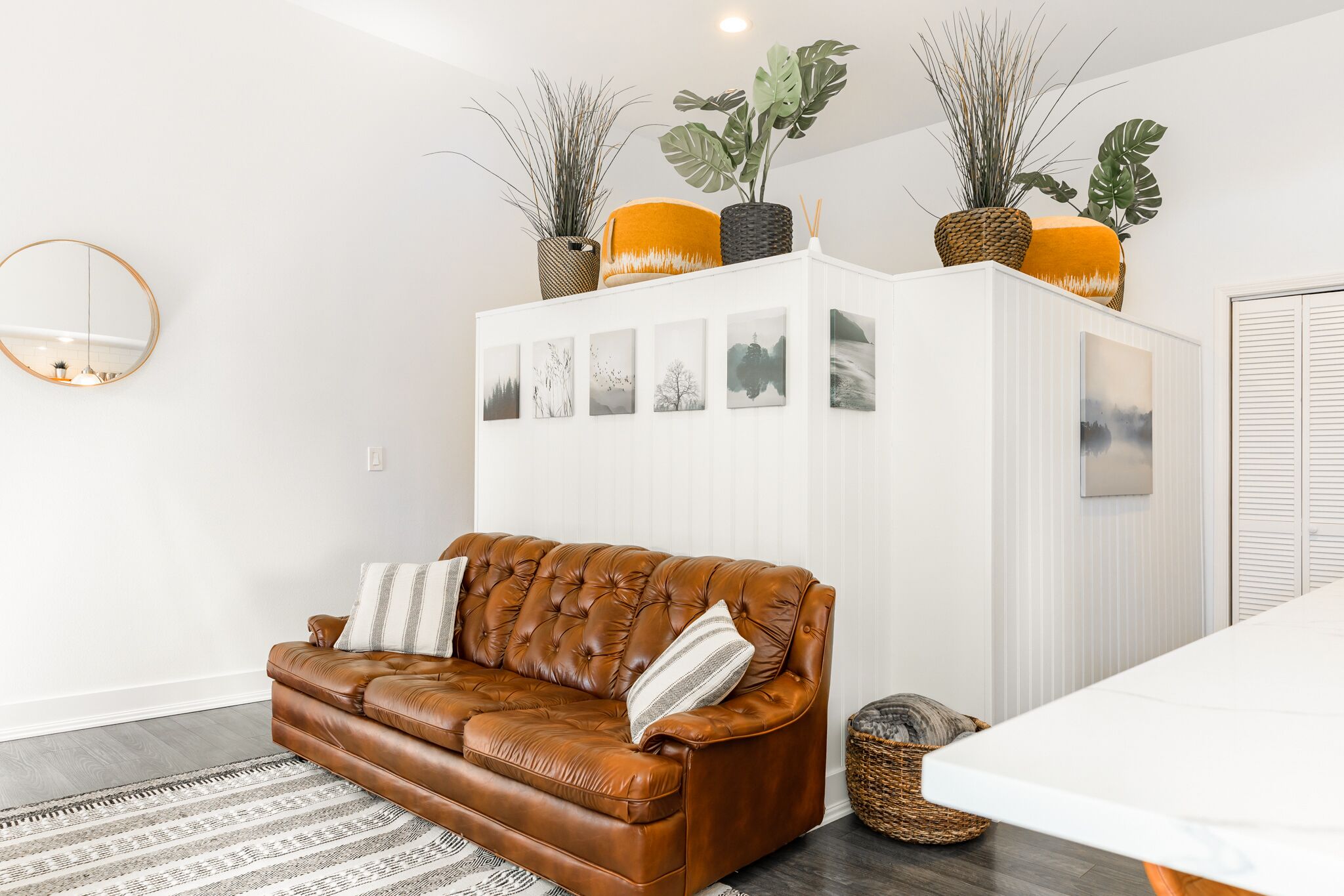 Un salon moderne avec un canapé en cuir marron, un meuble blanc orné de cadres et un grand miroir au mur.