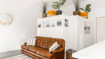 Un salon moderne avec un canapé en cuir marron, un meuble blanc orné de cadres et un grand miroir au mur.