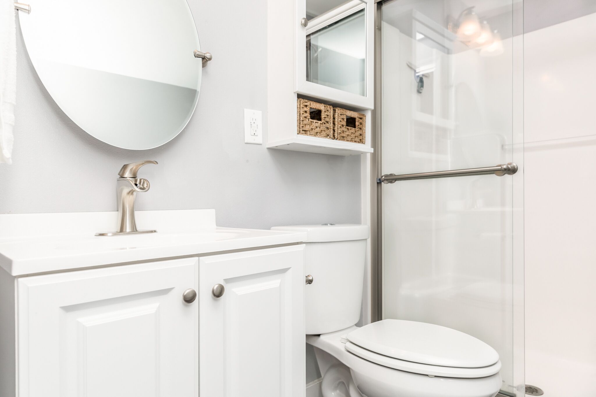 Une salle de bain moderne avec un lavabo blanc, un miroir rond et une cabine de douche en verre.