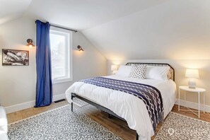 A bedroom with a bed, two bedside lamps, a window with a curtain, and a wall-mounted picture. - Strathcona. Sleeps 6. Steps from Whyte Ave. (Edmonton)