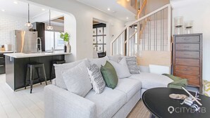 Een moderne woonkamer met een grijze bank, een zwarte salontafel en een trap naar een hoger gelegen verdieping.