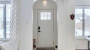 Een witte deur met een klein raam erboven, een hartvormige decoratie aan de muur en een patroon gordijn aan de linkerkant.