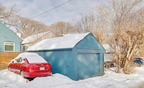 A red car parked in front of a blue garage with snow on the roof and surrounding ground. - Strathcona. Sleeps 6. Steps from Whyte Ave. (Edmonton)