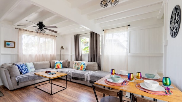 A living room with a sofa, coffee table, and dining table set with colorful glassware. - Somewhere Over Rainbow Loft - Hilo NEW (Hilo)