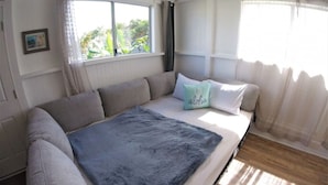 A bedroom with a large bed, a window with curtains, and a view of greenery outside. - Somewhere Over Rainbow Loft - Hilo NEW (Hilo)