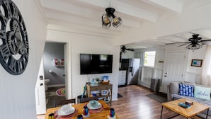 A spacious living area with a dining table set for four, a television, and a kitchen in the background. - Somewhere Over Rainbow Loft - Hilo NEW (Hilo)