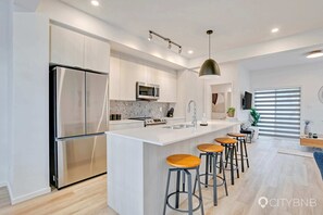 A modern kitchen with stainless steel appliances, a marble backsplash, and a central island with bar stools.