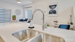 Une cuisine moderne dotée d’un évier à deux bacs, d’un grand îlot central et d’un coin repas avec une chaise bleue.