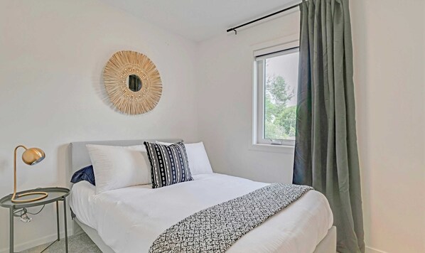 A bedroom with a bed, a round wall decoration, a bedside table with a lamp, and a window with curtains.