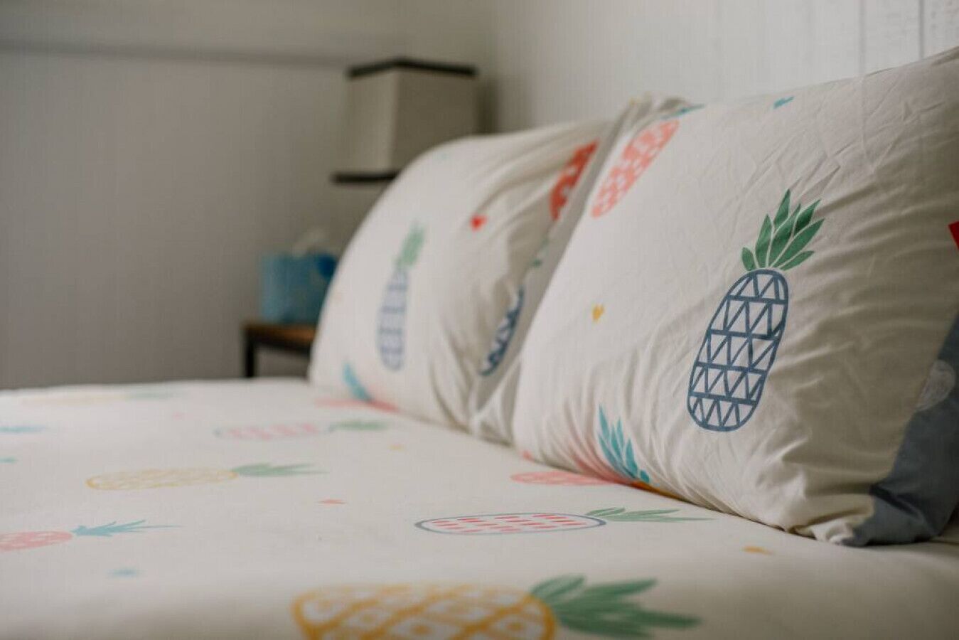 Un lit recouvert d’un drap blanc orné de motifs représentant des ananas et des oranges.