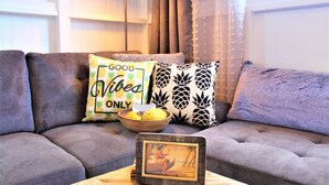 A living room with a grey sofa, two patterned throw pillows, a wooden coffee table with a framed picture, and a bowl of fruit. - Pineapple Loft - Downtown Hilo wAC (Hilo)