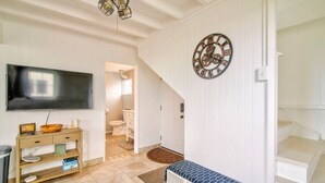A spacious living room with a large flat-screen TV, wooden console table, and a blue patterned bench. - Pineapple Loft - Downtown Hilo wAC (Hilo)