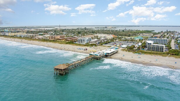 A coastal cityscape with a pier extending into the ocean, beachfront hotels, and a clear sky. - Ocean Front, Family Friendly Condo at Ola Grande (Cocoa Beach)