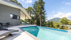 A modern pool area with lounge chairs and a view of trees and hills. - Treetops Retreat: A Serene Rainforest Escape with Mountain Views (Brinsmead)