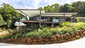 A modern house with a glass balcony, surrounded by a rock garden and lush greenery. - Treetops Retreat: A Serene Rainforest Escape with Mountain Views (Brinsmead)