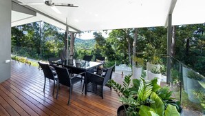 A modern outdoor dining area with a table and chairs, surrounded by potted plants and overlooking a lush landscape. - Treetops Retreat: A Serene Rainforest Escape with Mountain Views (Brinsmead)