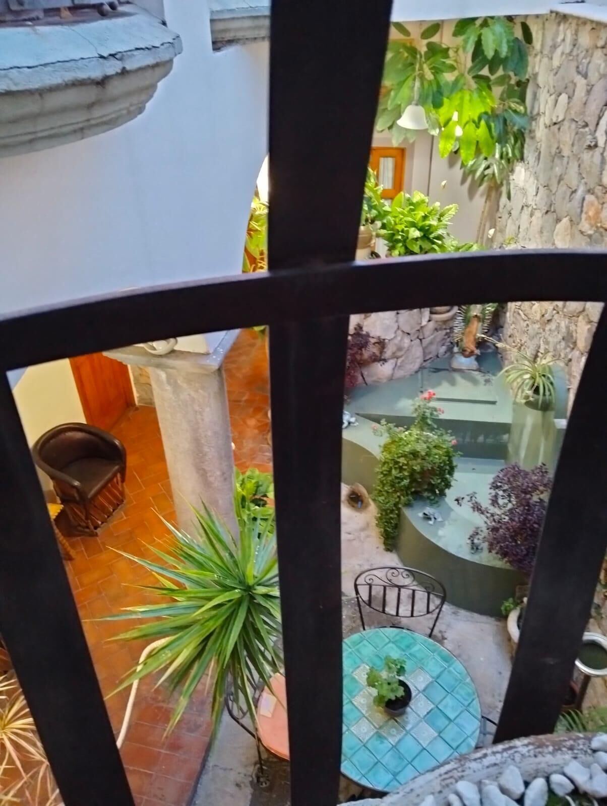 A courtyard with a stone wall, potted plants, a round table, and a chair.