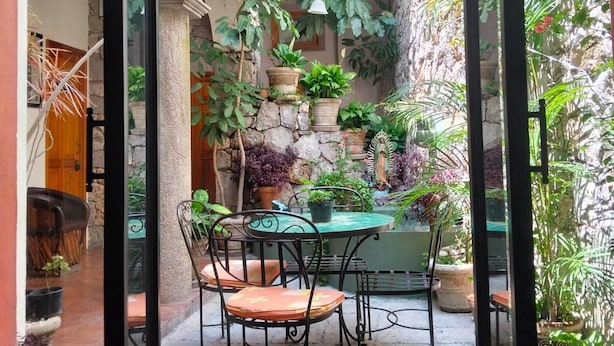 An outdoor patio with a table and chairs, surrounded by potted plants and a stone wall.