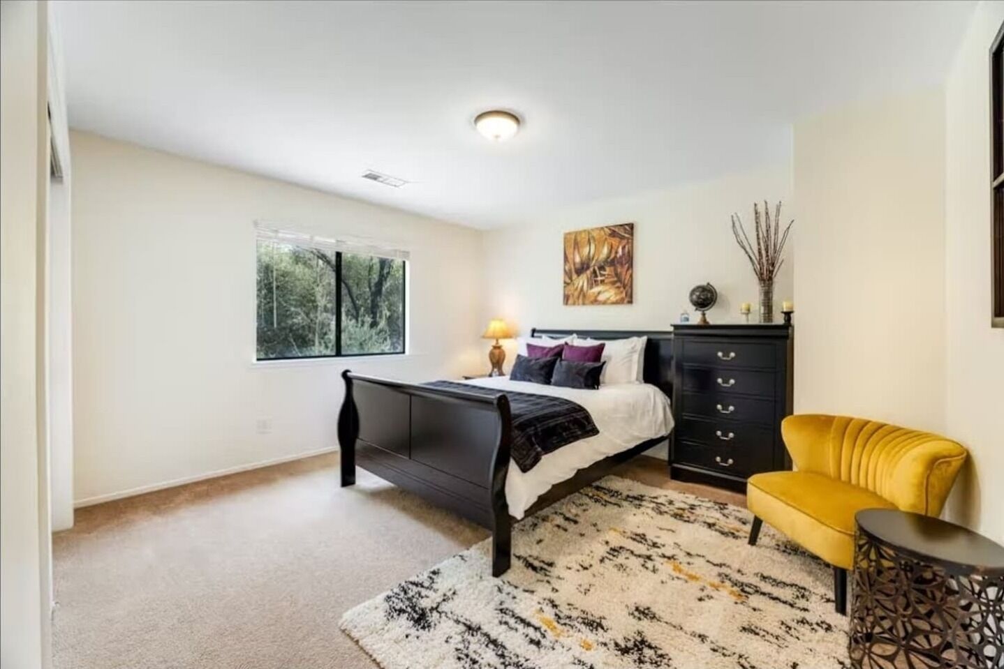 A bedroom with a bed, a desk, a chair, a dresser, and a window with a view of trees.