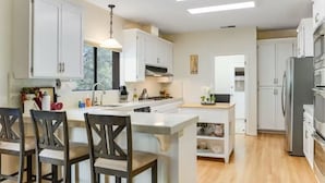 A modern kitchen with white cabinets, a central island, and a dining area with wooden chairs.
