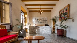 A lobby with a reception desk, a red sofa, a wooden table, and potted plants. - Hotel Meson de Isabel (Querétaro)