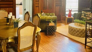 Una sala de estar acogedora, con piso de madera, zona de comedor, sofá verde y una araña.