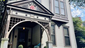 Una casa de estilo victoriano con un porche delantero destacado, un gran ventanal saliente y una puerta principal decorativa.