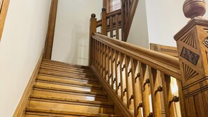 Una escalera de madera con barandilla y balaustres, que conduce a un rellano con un ventanal con persianas.