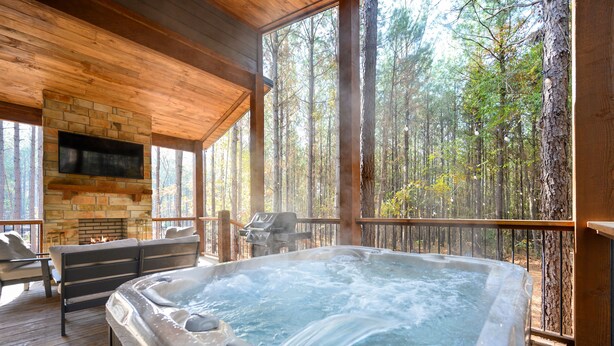 Ein Whirlpool auf einer Holzterrasse mit Kamin aus Stein und Sitzgelegenheiten im Freien.