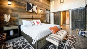 Ein Schlafzimmer mit Holzbalkendecke, einem Bett mit weißer Bettwäsche, einer Sitzbank und einem geometrischen Teppich.