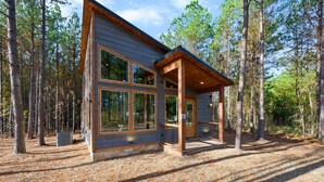 Eine moderne Holzhütte mit großen Fenstern, einer Holzterrasse und einem Wald im Hintergrund.
